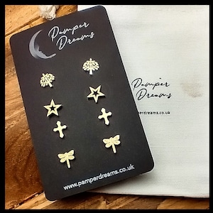 May include: A black card with the text "Pamper Dreams" and a moon design. The card has a variety of gold glitter designs including a tree, star, cross, and dragonfly. The card is displayed on a white fabric bag with the text "Pamper Dreams" and "pampdrems.co.uk".
