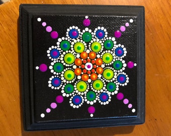 small mandala bright colored dot painting on canvas and mounted on a 4 inch by 4 inch square frame on a black background