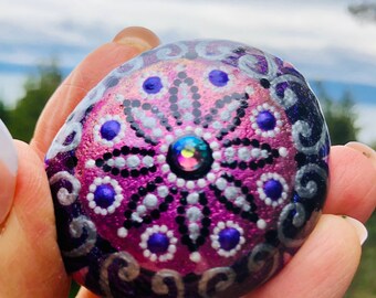 Hand painted mandala rock in metallic purple, pinks, black and white and sealed with resin for everlasting beauty.