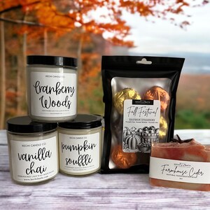 May include: An assortment of fall-themed bath and body products. Includes three glass jar candles labeled "Cranberry Woods", "Vanilla Chai", and "Pumpkin Souffl&eacute;". Also shown are shower steamers and a bar of "Farmhouse Cider" soap.