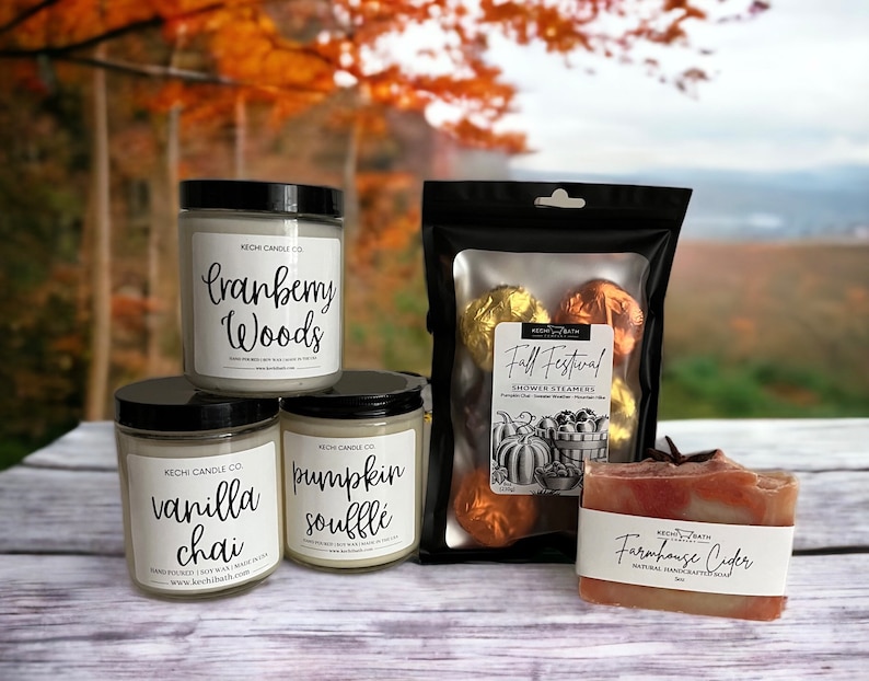 May include: An assortment of fall-themed bath and body products. Includes three glass jar candles labeled "Cranberry Woods", "Vanilla Chai", and "Pumpkin Souffl&eacute;". Also shown are shower steamers and a bar of "Farmhouse Cider" soap.