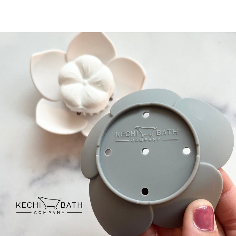 May include: Gray silicone bath flower with five petals and five holes. The center of the flower has the text "KECHI BATH COMPANY" with a small bathtub icon.