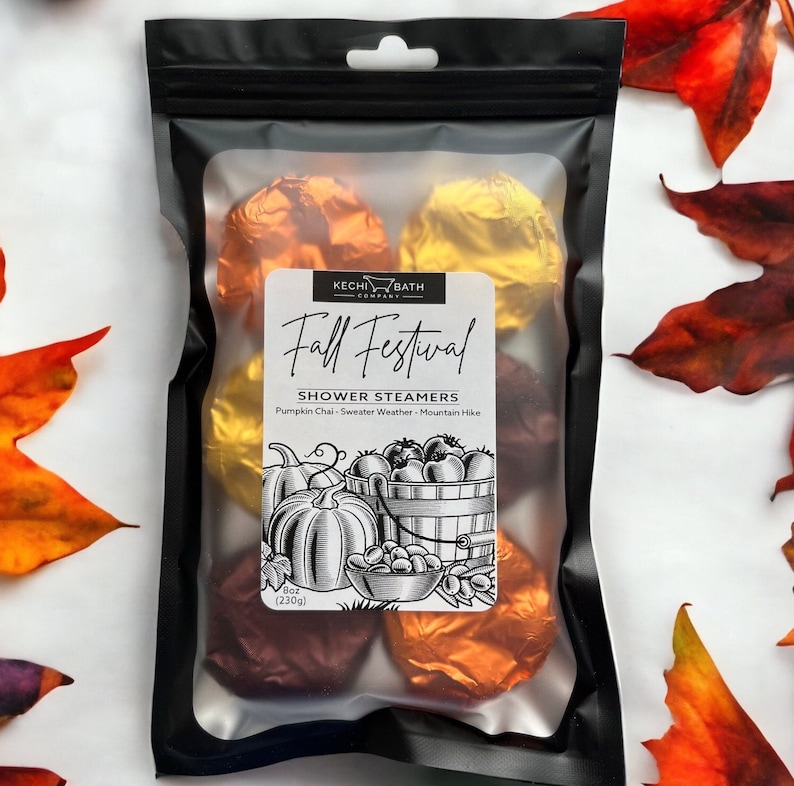 May include: A black package containing shower steamers wrapped in orange and gold foil. The label reads "Fall Festival" with illustrations of pumpkins and a basket of fruit. The package weighs 8 oz (230g).