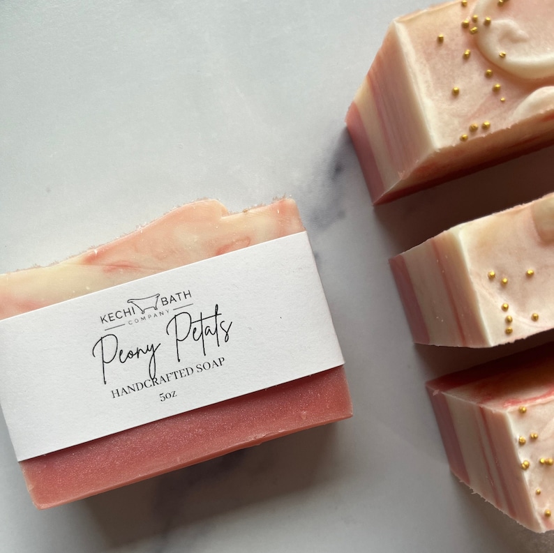 Puede incluir: Barras de jab&oacute;n artesanales con un dise&ntilde;o en espiral rosa y blanco, etiquetadas como "Peony Petals". Las barras de jab&oacute;n pesan 142 g y est&aacute;n decoradas con motas doradas. El jab&oacute;n es de Kechi Bath Company.