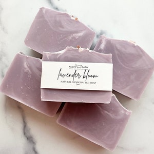 May include: Four bars of lavender-scented soap, each with a swirl pattern. The soap is a light purple color and has a label that reads "Kechi Bath Company Lavender Bloom Natural Handcrafted Soap 5oz".