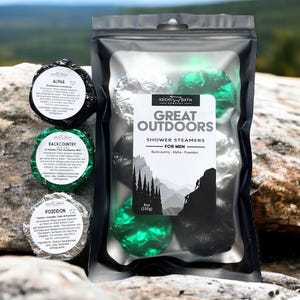 May include: A black pouch with a clear front containing six black and green shower steamers. The pouch has a white label that reads "Great Outdoors Shower Steamers for Men Backcountry - Alpha - Poseidon" and a smaller label that reads "Box (230g)". Three individual shower steamers are visible outside the pouch, each with a black and white label.