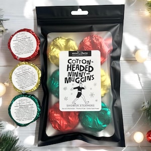 May include: A black bag containing shower steamers wrapped in red, green, and gold foil. The bag has a label that reads "Cotton-Headed Ninny-Muggins" and "Shower Steamers." Three individual shower steamers are visible to the left, each in foil.