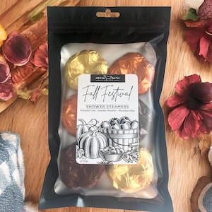 May include: A black bag containing shower steamers. The bag has a label that reads "Fall Festival" and "Shower Steamers". The steamers are wrapped in gold, copper, and burgundy foil. The label also features illustrations of pumpkins and a basket of fruit.