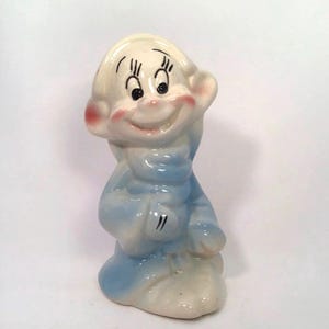 May include: A ceramic figurine of a cartoon character with a blue and white outfit and a big smile. The character has large eyes and a pointed hat.