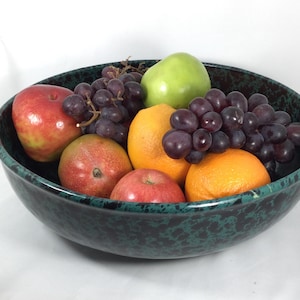 May include: A green and black speckled bowl filled with fruit, including red apples, oranges, a green apple, and grapes.