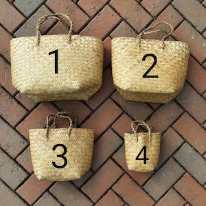 May include: Four woven straw tote bags of varying sizes, each with a braided handle. The bags are numbered 1 through 4 in black. The bags are displayed on a brick surface.