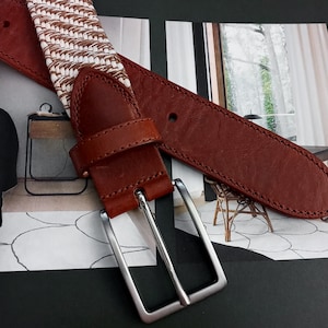 以下が含まれることがあります： 白と茶色の織り模様のストラップと銀色のバックルが付いた茶色の革製のベルト