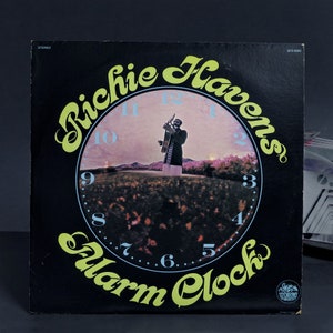 May include: A black vinyl record album cover with a yellow and green clock face featuring Richie Havens and the title "Alarm Clock".