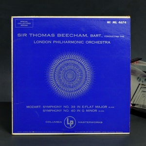 May include: A blue vinyl record album cover with a white circular design in the center. The album features Sir Thomas Beecham conducting the London Philharmonic Orchestra in Mozart's Symphony No. 39 in E-Flat Major and Symphony No. 40 in G Minor. The album is part of the Columbia Masterworks series.