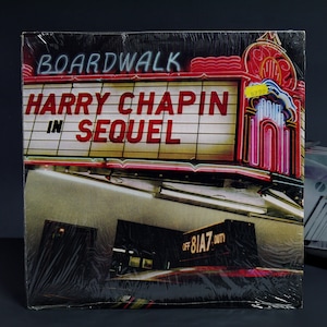 May include: A vintage vinyl record album cover featuring a neon sign for "Boardwalk" with the text "Harry Chapin in Sequel" on the marquee. The album cover is wrapped in plastic.