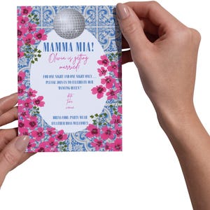 Op de afbeelding: Een rechthoekige uitnodigingskaart met een discobal-afbeelding en de woorden "MAMMA MIA! Olivia gaat trouwen!" in een decoratief lettertype. De kaart heeft een bloemenrand met roze bloemen en een blauw-wit tegelpatroon.