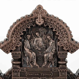 May include: A bronze-coloured religious icon depicting the Holy Trinity. The icon features three figures seated on a throne, with a cross above them. The inscription at the bottom reads "Святая Троица" which translates to "Holy Trinity" in English.