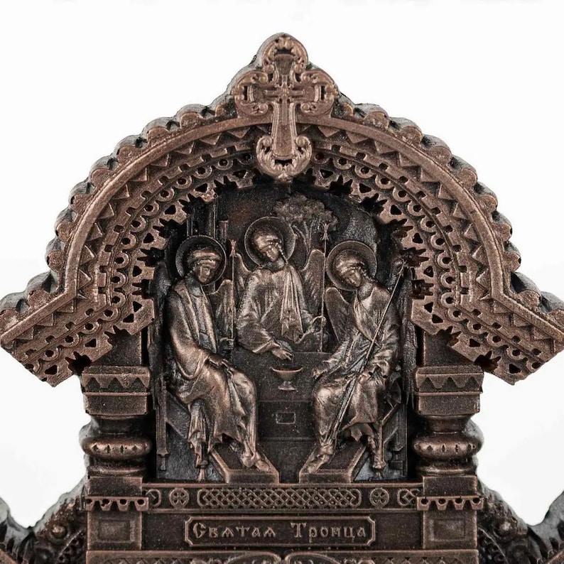 May include: A bronze-coloured religious icon depicting the Holy Trinity. The icon features three figures seated on a throne, with a cross above them. The inscription at the bottom reads "Святая Троица" which translates to "Holy Trinity" in English.