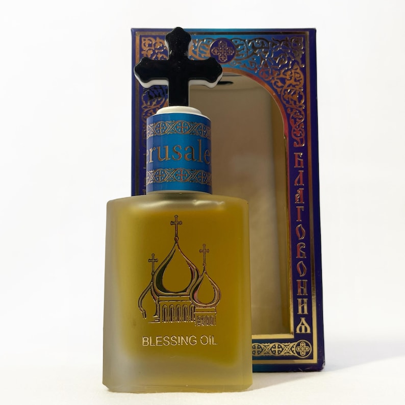 May include: A square, frosted glass bottle of Blessing Oil with a black cross-shaped stopper. The bottle features a gold illustration of church domes and the text "BLESSING OIL". The blue and gold box is visible in the background.