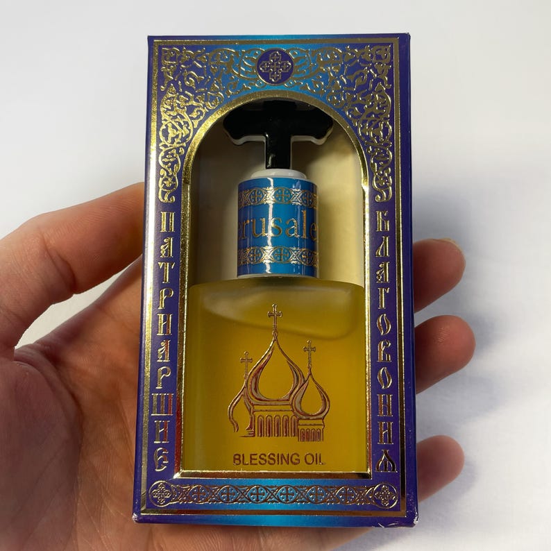 May include: A bottle of Blessing Oil in a decorative box. The box is blue and gold with ornate designs and text in a foreign language. The bottle has a gold liquid and a label that says "Jerusalle".
