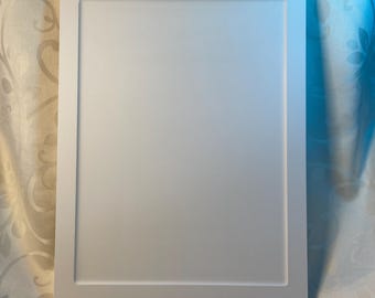 May include: A white picture frame with a raised border. The frame is made of wood and has a smooth finish.