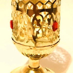 May include: A gold metal candle holder with a glass insert and red glass accents. The holder has a decorative, ornate design.