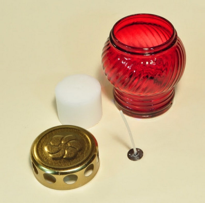 May include: A red glass votive candle holder with a white candle, a gold metal lid with a decorative design, and a white wick.