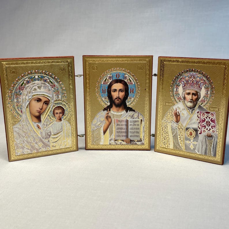 K&ouml;nnte beinhalten: Ein Satz von drei goldgerahmten religi&ouml;sen Ikonen. Die Ikonen zeigen die Jungfrau Maria und das Kind, Jesus Christus und einen Heiligen. Die Ikonen sind durch eine Kette miteinander verbunden.
