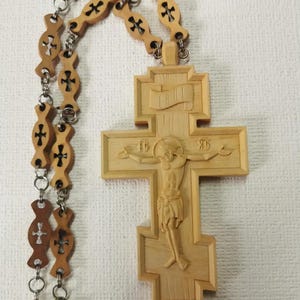 Könnte beinhalten: Ein Holzkreuz mit einer geschnitzten Jesus Christus-Figur. Das Kreuz ist an einer Kette aus Holz und Metall befestigt.
