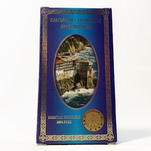 May include: A rectangular box with a dark blue background and gold trim. The front features an oval image of a building on a cliff overlooking the sea. Text reads "Essential Greek Oils 100% Pure".