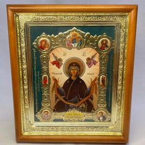 Puede incluir: Icono religioso enmarcado en madera dorada. Presenta una figura central con aureola, rodeada de detalles dorados y una escena religiosa sobre fondo verde. El conjunto está adornado con motivos complejos.