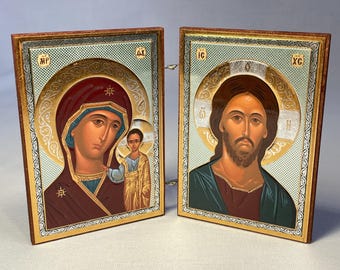 May include: Two religious icons depicting figures with halos, set in ornate gold-trimmed frames. One shows a woman and child, the other a man with a beard. The icons are hinged together.