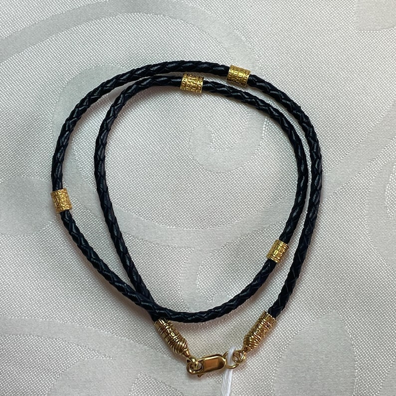 May include: A black leather cord necklace with gold accents. The cord is braided and has a clasp closure.