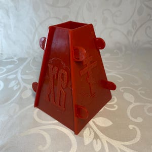 May include: Red plastic mould for making a traditional Easter cake. The mould has a cross and Cyrillic letters on the sides.