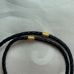 May include: A black leather cord necklace with two gold-toned metal beads.