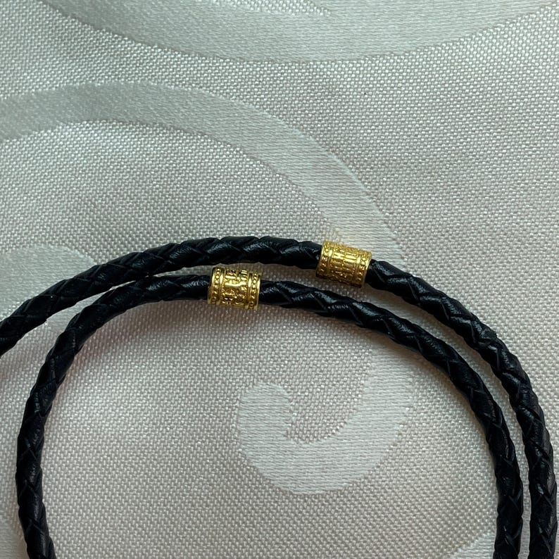 May include: A black leather cord necklace with two gold-toned metal beads.