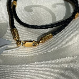 May include: A black leather necklace with gold accents. The necklace has a braided design and a clasp closure.