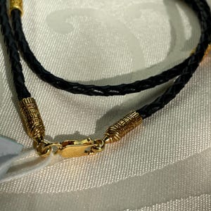 May include: A black leather braided necklace with gold-toned clasps and decorative end pieces.