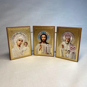 K&ouml;nnte beinhalten: Ein Satz von drei goldgerahmten religi&ouml;sen Ikonen. Die Ikonen zeigen die Jungfrau Maria und das Kind, Jesus Christus und einen Heiligen. Die Ikonen sind in Gold gerahmt und haben einen dekorativen Rand.