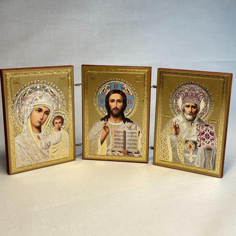 K&ouml;nnte beinhalten: Ein Satz von drei goldgerahmten religi&ouml;sen Ikonen. Die Ikonen zeigen die Jungfrau Maria und das Kind, Jesus Christus und einen Heiligen. Die Ikonen sind auf einem Holzst&auml;nder montiert.