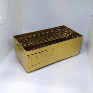 May include: A gold metal rectangular planter with an embossed floral design. The planter has two handles on the sides.