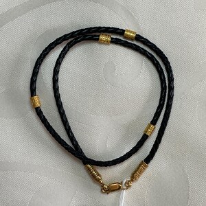 May include: A black leather necklace with gold accents. The necklace is braided and has a clasp closure.