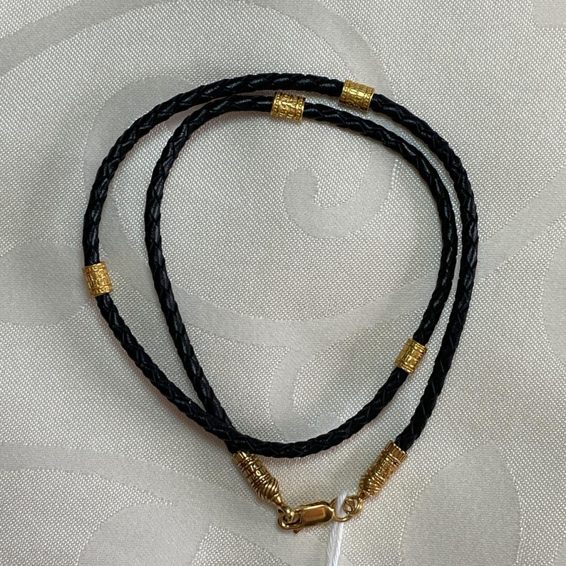 May include: A black leather necklace with gold accents. The necklace is braided and has a clasp closure.