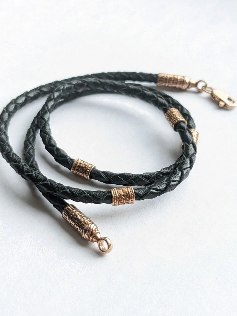 May include: A black leather cord necklace with gold-toned metal accents. The cord is braided and has a clasp closure.