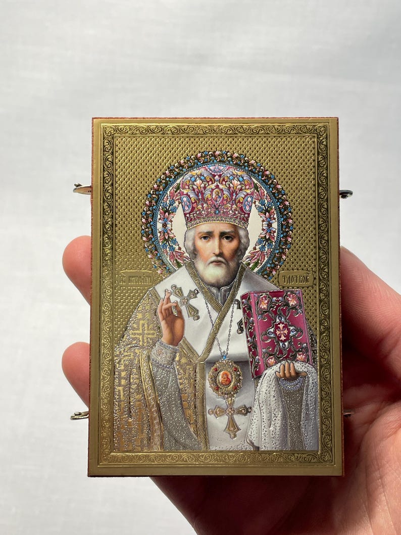 K&ouml;nnte beinhalten: Eine goldgerahmte Ikone, die eine religi&ouml;se Figur mit wei&szlig;em Bart und Krone darstellt. Die Figur h&auml;lt ein Buch und ein Kreuz. Die Ikone ist von einem dekorativen Rahmen umgeben.