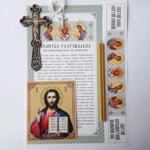 Puede incluir: Artículos religiosos que incluyen un crucifijo plateado, un pequeño icono de Jesucristo y una tarjeta de oración con texto en idioma extranjero. También se incluye una vela amarilla. Los artículos están conectados con un hilo blanco.