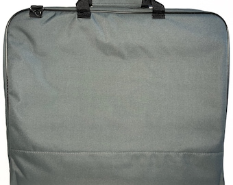 Puede incluir: Una funda para ropa rectangular de color gris carbón que cuenta con un asa superior con agarre acolchado, correas de nailon negro y un anillo en D de metal en la esquina superior izquierda. El exterior es de tela lisa y de color sólido.