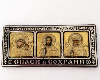 May include: A rectangular religious icon with three panels. Each panel features a gold-toned image of a religious figure. The icon has a black border with ornate detailing and the text "СПАСИ и СОХРАНИ" in the center.
