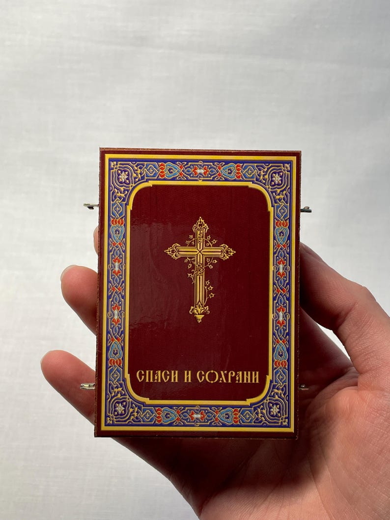 K&ouml;nnte beinhalten: Eine kleine, rechteckige Schachtel in Rot mit einem goldenen Kreuz und einem verzierten Rand. Die Schachtel tr&auml;gt den Text "СПАСИ И СОХРАНИ" in goldenen Buchstaben.