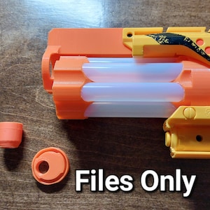 Puede incluir: Una pistola de juguete amarilla y naranja con un cañón de plástico transparente y un diseño a rayas negro y amarillo. La pistola está desmontada y las piezas están dispuestas sobre una superficie de madera. La pistola tiene una pequeña tapa naranja y un pequeño anillo naranja.